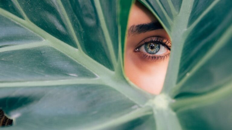 woman peeking over green leaf plant taken at daytime